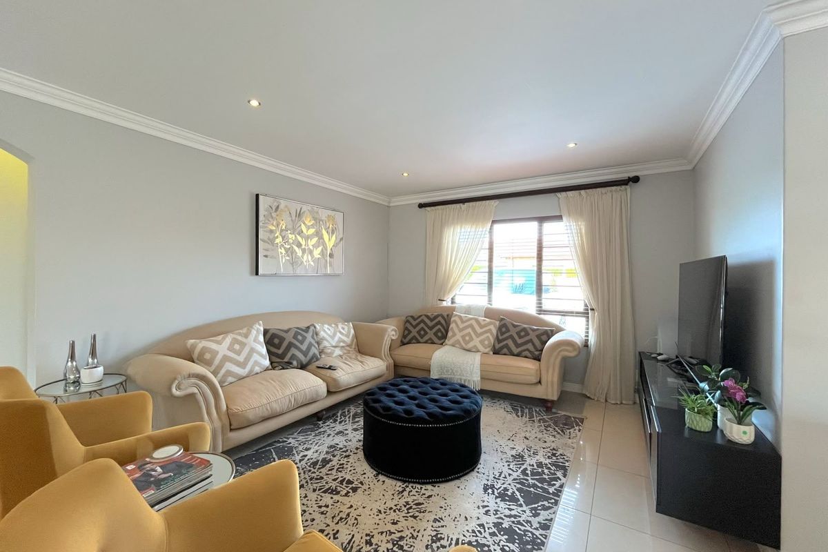 A well-maintained living room featuring neutral tiled flooring, recessed downlighting, and decorative crown molding, providing a bright and comfortable space.