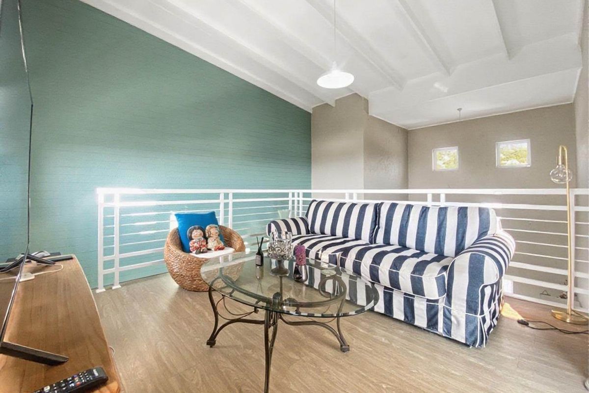 A bright living area featuring a vaulted ceiling with exposed beams, laminate flooring, and a protective metal balustrade overlooking the lower level.