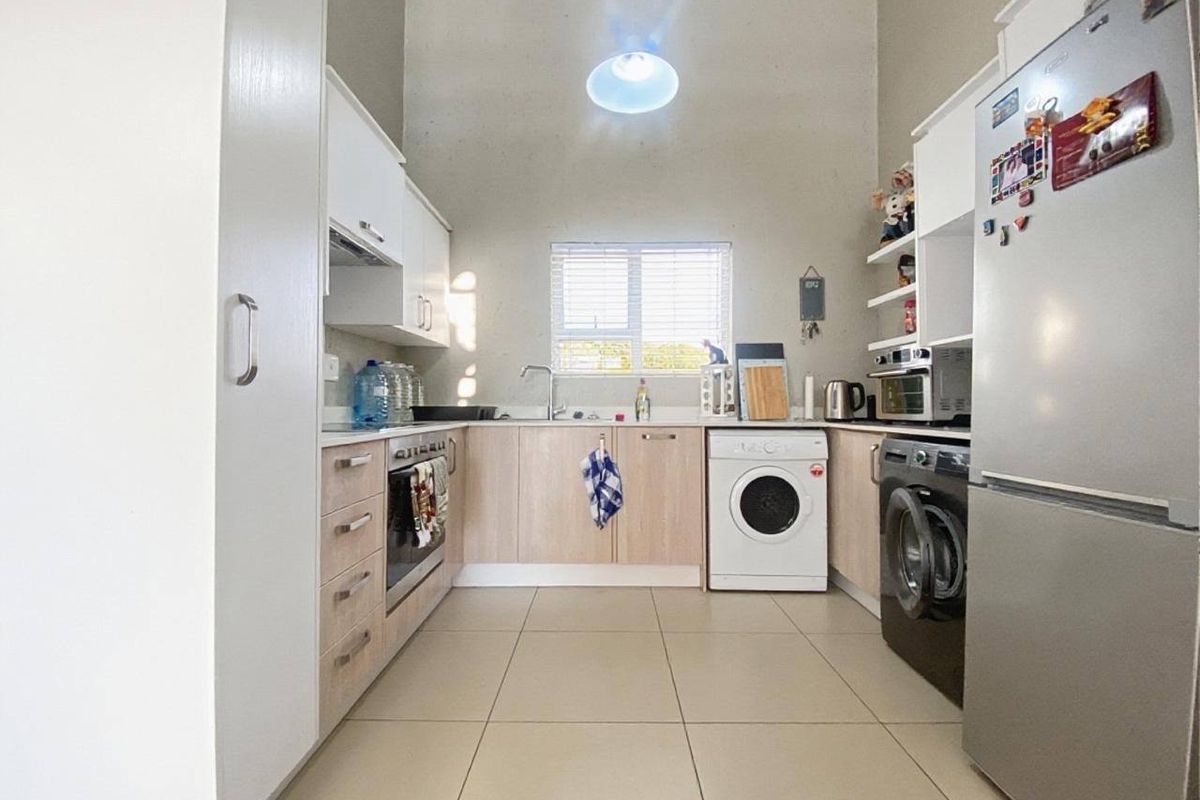 A functional kitchen featuring light wood-finish cabinetry, tiled flooring, built-in oven, and integrated laundry appliance space under the countertop.