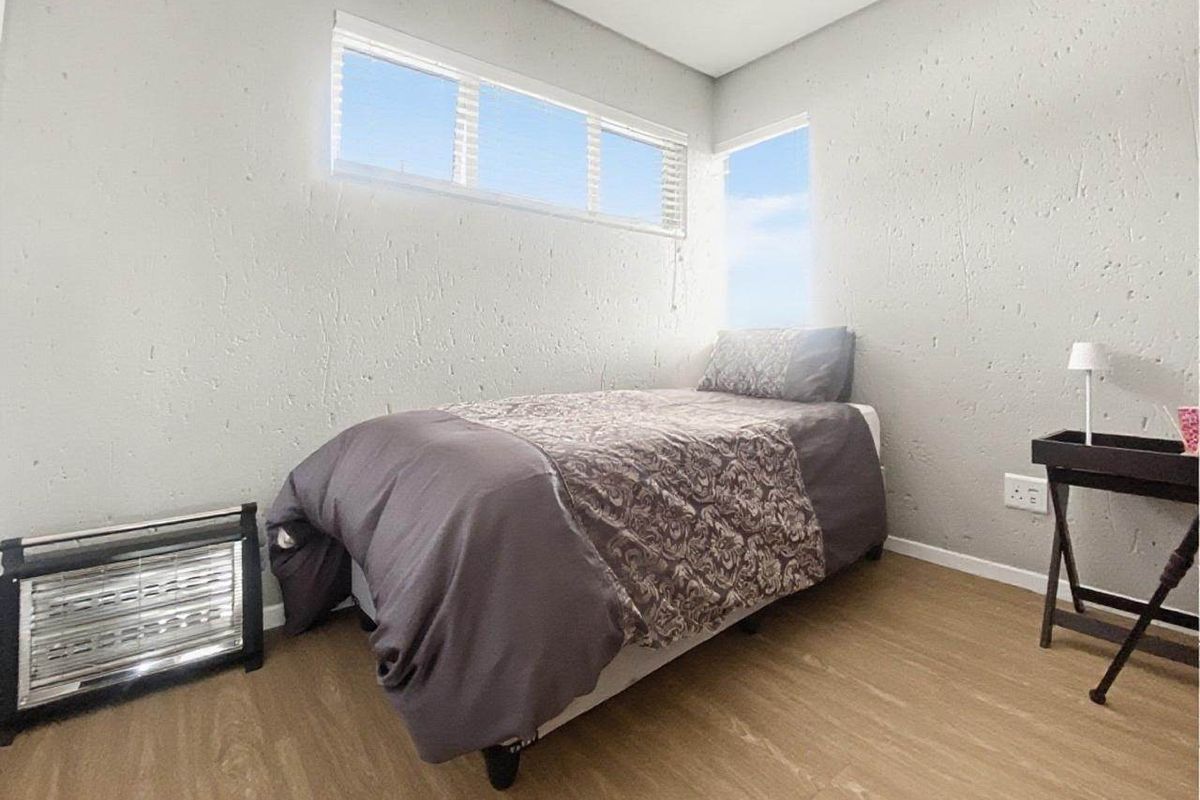 A compact bedroom featuring textured walls, laminate flooring, and horizontal window blinds, providing a neutral and functional living space.