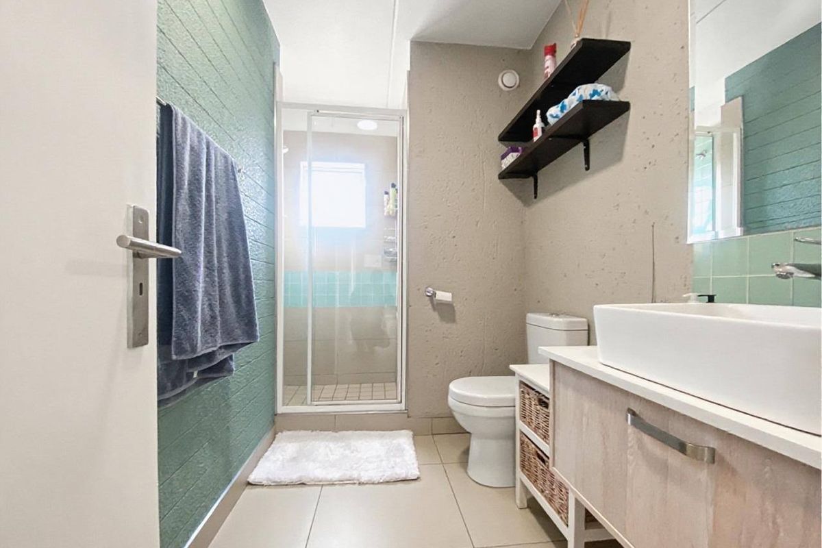 A modern bathroom featuring a glass shower enclosure, a vessel sink vanity, and a neutral color palette with a green accent wall.