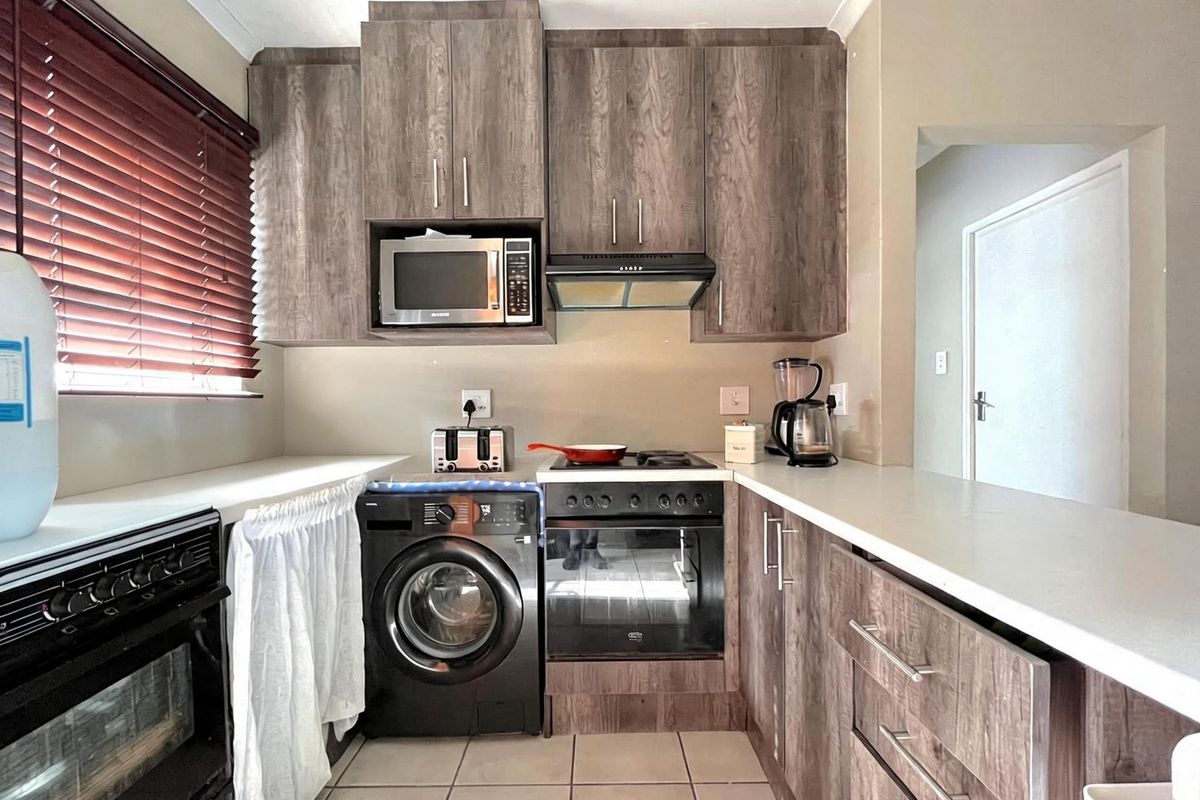A functional kitchen featuring wood-look cabinetry, laminate countertops, built-in oven with hob, extractor fan, and integrated microwave, complemented by tiled flooring.