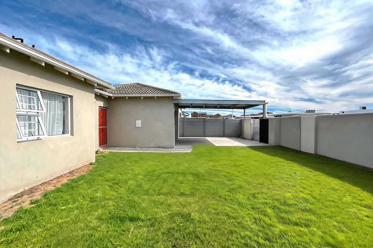 A well-maintained rear garden featuring a level lawn, a paved carport area, and secure boundary walls.