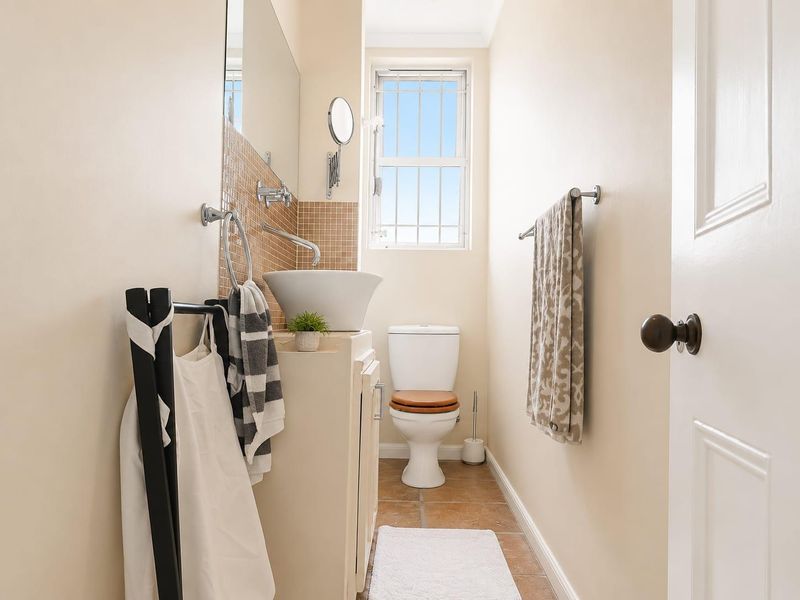 A compact bathroom featuring a vessel sink on a vanity cabinet, mosaic tile backsplash, and a standard toilet with tiled flooring.