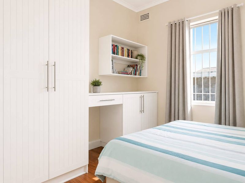 A well-maintained bedroom featuring built-in cabinetry, a dedicated desk area, timber flooring, and a window with security bars.