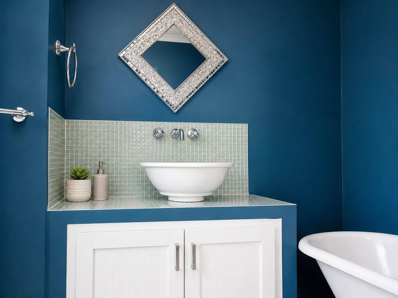 A modern bathroom featuring a white vessel sink on a vanity cabinet with a mosaic tile backsplash and a freestanding bathtub.
