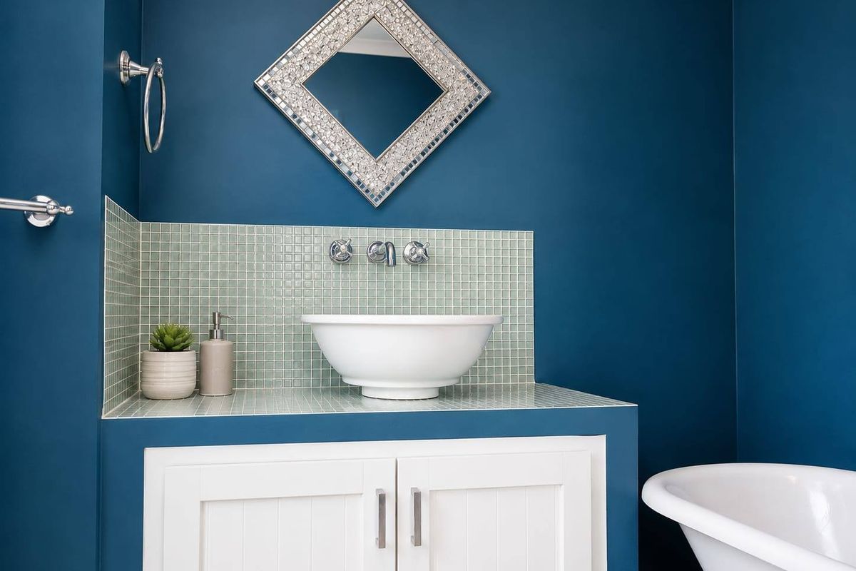 A modern bathroom featuring a white vessel sink on a vanity cabinet with a mosaic tile backsplash and a freestanding bathtub.