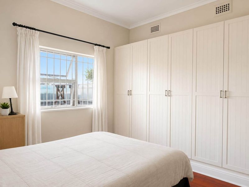 A well-maintained bedroom featuring extensive built-in wardrobes, timber flooring, and a window fitted with security bars.