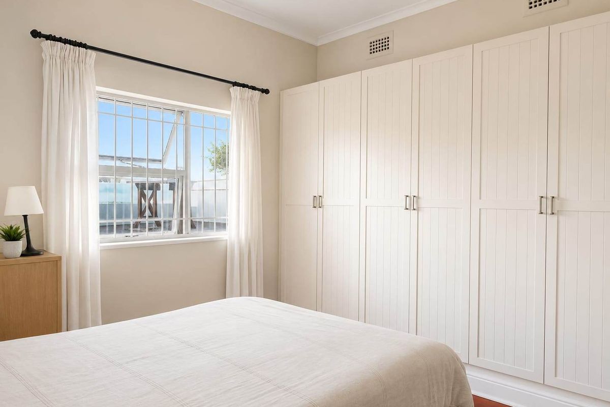 A well-maintained bedroom featuring extensive built-in wardrobes, timber flooring, and a window fitted with security bars.