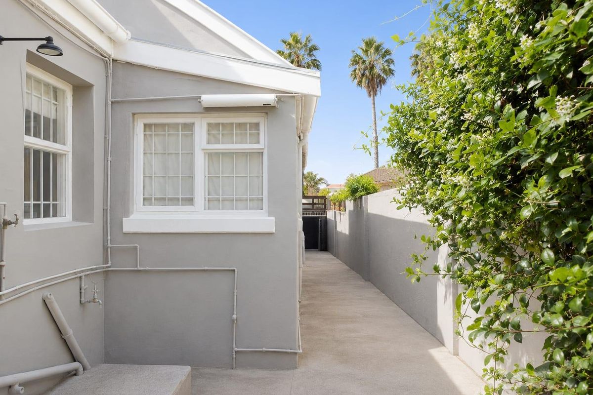 A clean and well-maintained side passage featuring a concrete walkway, boundary wall, and exterior lighting, providing access to the rear of the property.