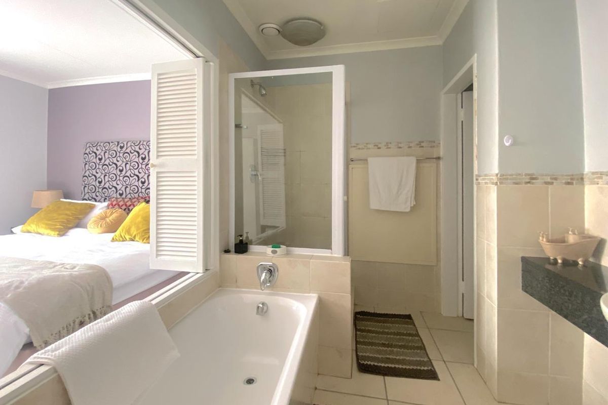 Bathroom featuring a built-in bathtub, separate glass shower enclosure, and tiled finishes, with an open-plan connection to the adjacent bedroom.