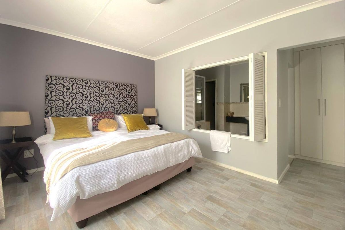 A well-maintained bedroom featuring tiled flooring, built-in cupboards, and a unique louvered shutter window opening into the adjacent bathroom.