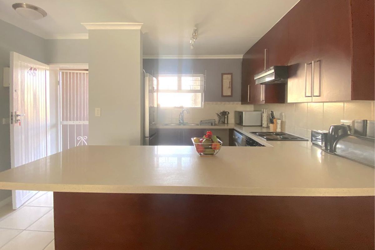 A functional kitchen featuring dark wood cabinetry, stone countertops, a breakfast bar, and integrated appliances, with direct access to an exterior security gate.