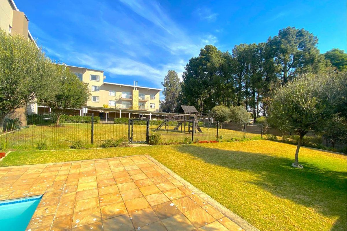 A well-maintained rear garden area featuring a stone patio, swimming pool, and communal playground equipment set against the apartment building facade.