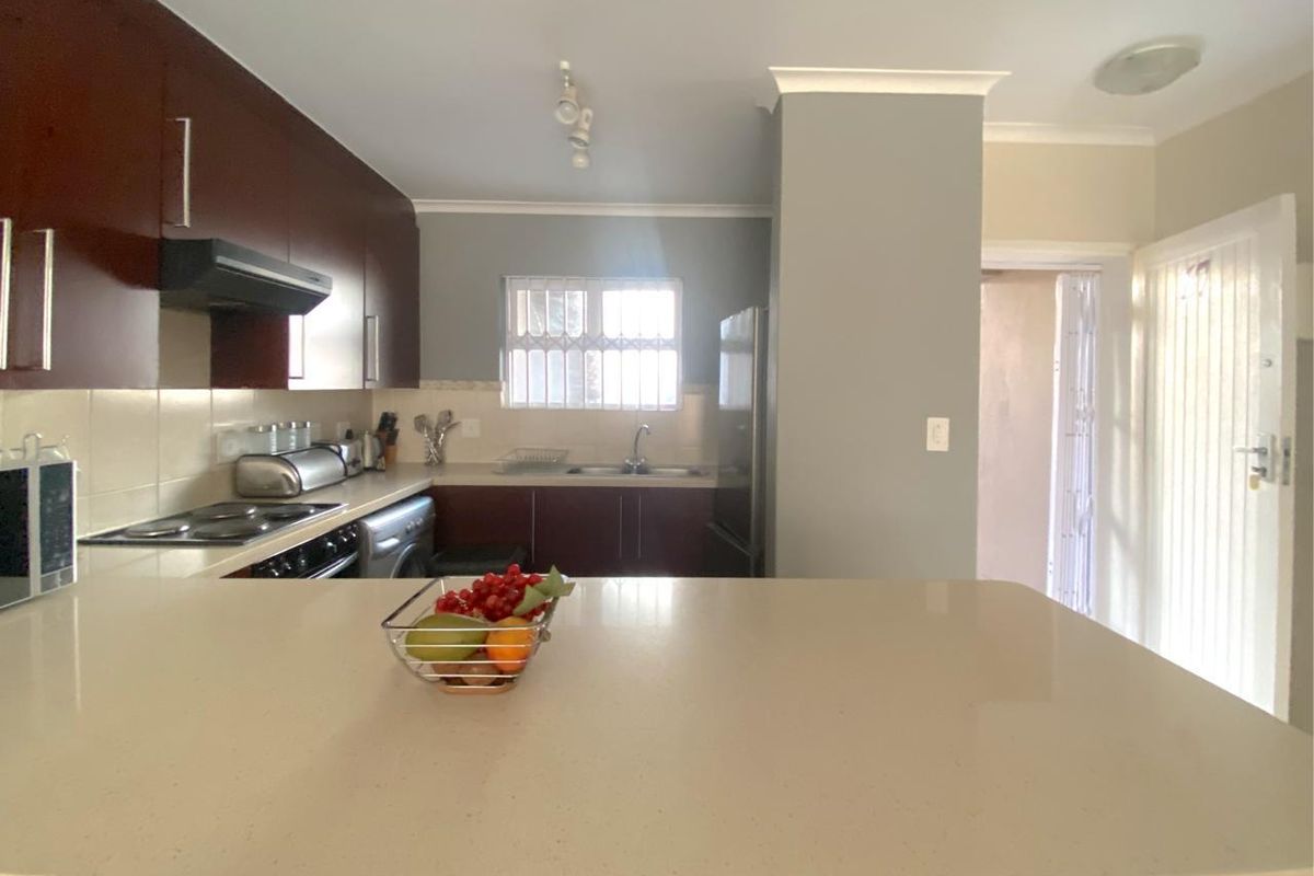 A functional kitchen featuring dark wood cabinetry, stone countertops, integrated appliances, and a breakfast bar area with neutral wall finishes.