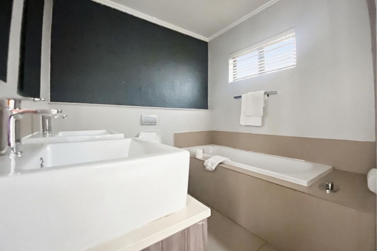 Modern bathroom featuring a built-in bathtub, dual vanity basins, and a concealed cistern toilet with neutral wall finishes.