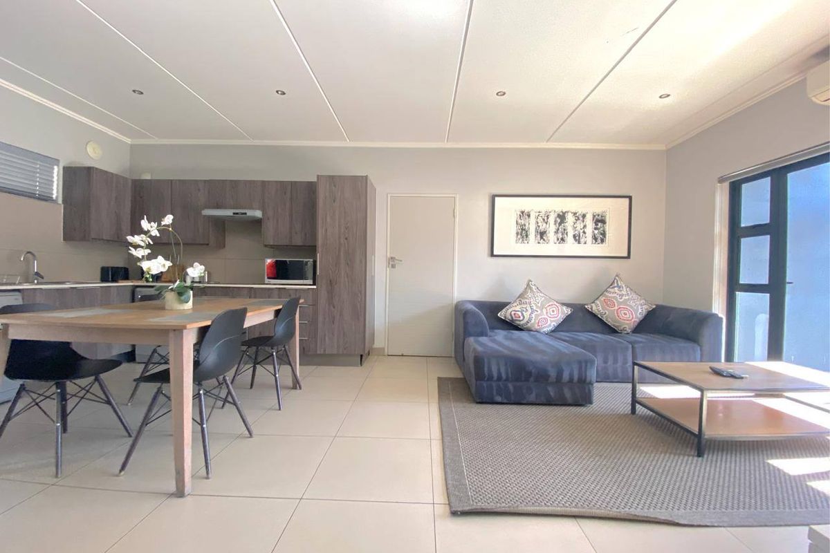 Modern open-plan living area featuring a contemporary kitchen with built-in cabinetry, tiled flooring, and seamless flow to the lounge space.