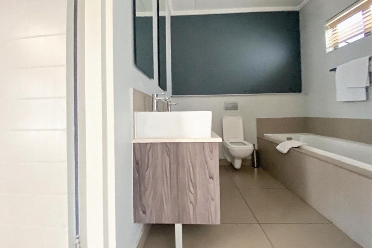 Modern bathroom featuring a wall-mounted vanity with a vessel sink, wall-hung toilet, and a built-in bathtub with neutral floor tiling.