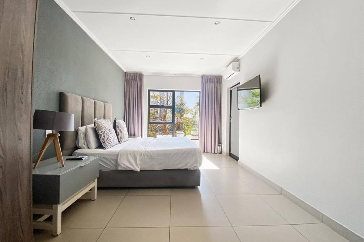 Spacious bedroom featuring neutral tiled flooring, a feature wall, air conditioning, and large windows allowing for ample natural light.