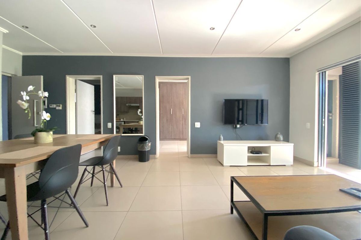 Spacious open-plan living and dining area featuring neutral tiled flooring, recessed lighting, and direct access to an outdoor balcony through sliding doors.