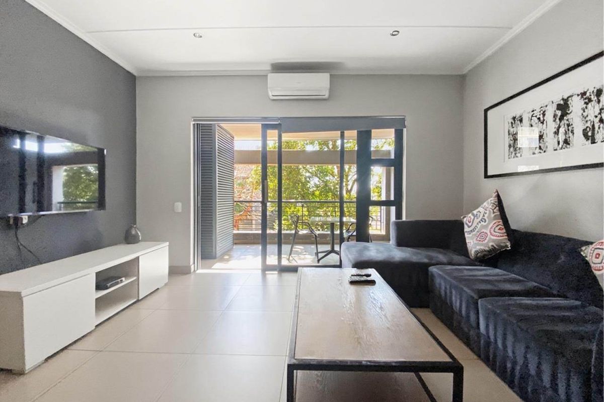 Modern living room featuring neutral tiled flooring, recessed lighting, a wall-mounted air conditioning unit, and direct access to a private balcony through sliding glass doors.