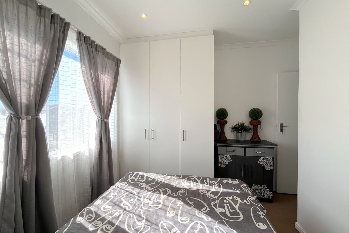 A well-maintained bedroom featuring built-in cupboards, recessed downlighting, and neutral finishes, offering a clean and functional living space.