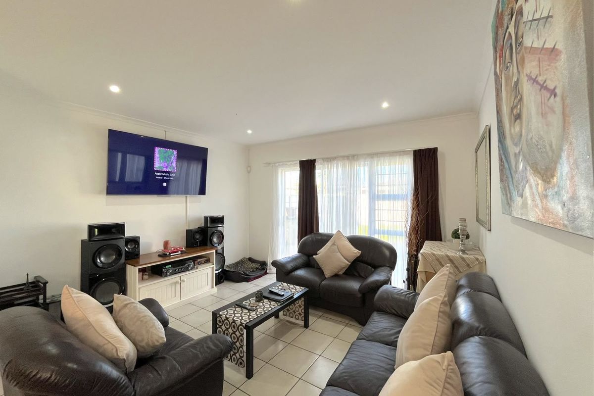 A well-maintained living room featuring neutral ceramic floor tiles, recessed downlighting, and a large sliding glass door providing natural light.