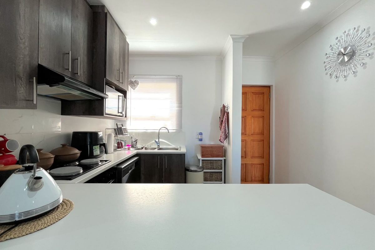 A functional kitchen featuring dark wood cabinetry, light countertops, stainless steel sink, and recessed lighting, providing a clean and practical workspace.