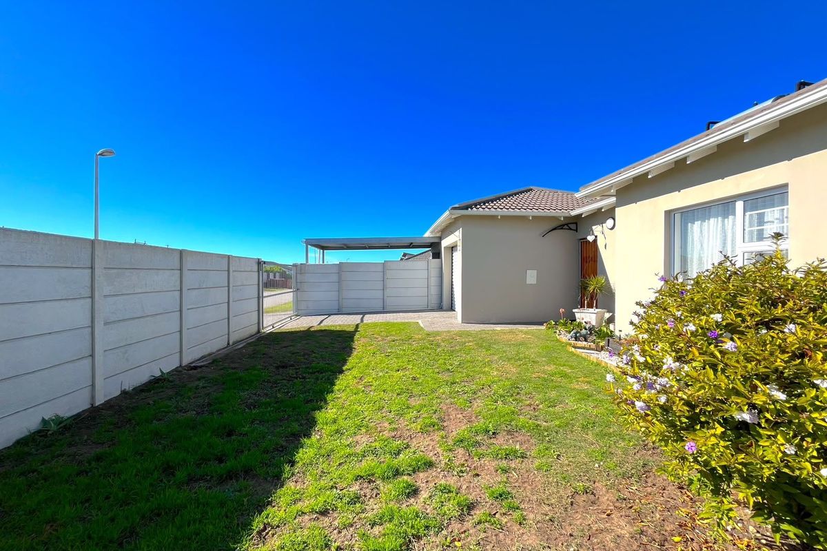 A rear exterior view of the property featuring a paved driveway, carport, and a private garden area enclosed by a precast concrete boundary wall.