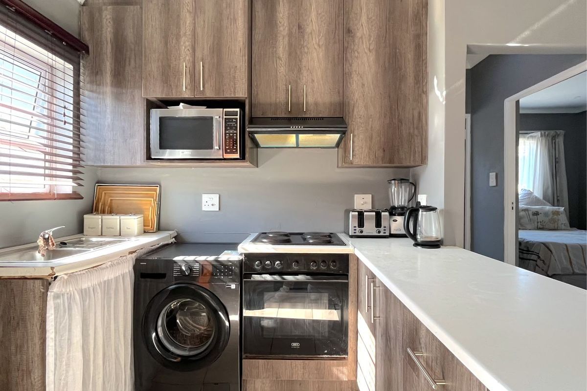Compact kitchen featuring wood-look cabinetry, built-in oven with electric hob, extractor fan, integrated microwave, and a stainless steel sink with tiled flooring.