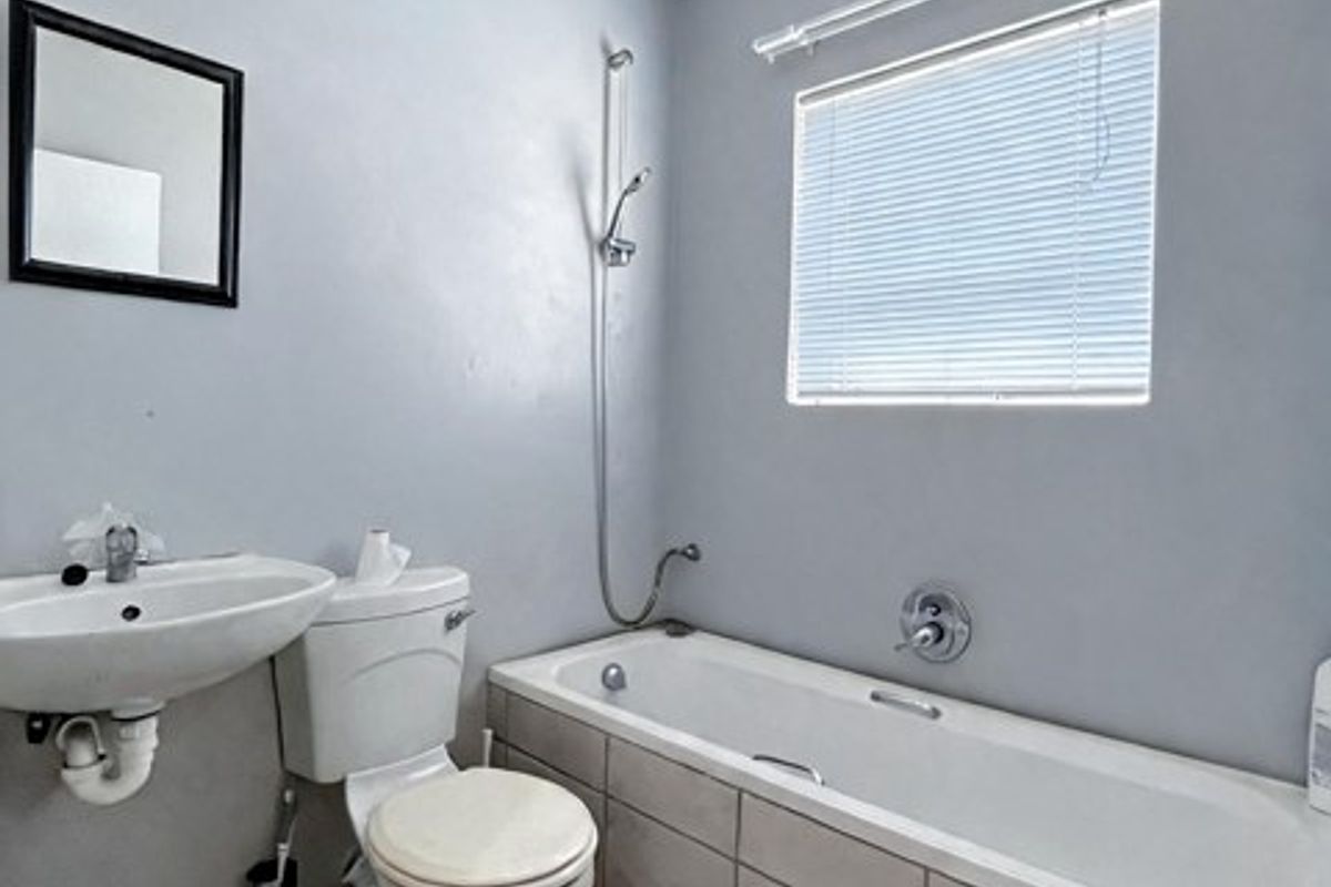 A functional bathroom featuring a bathtub with shower attachment, pedestal basin, toilet, and tiled flooring, offering a clean and practical layout.
