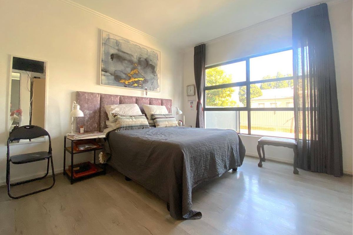 A bright bedroom featuring large windows that provide ample natural light, complemented by modern laminate flooring and neutral wall finishes.