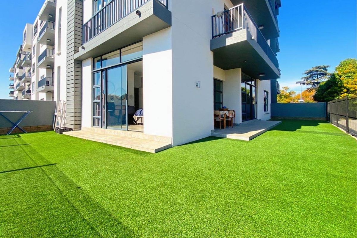 Modern apartment exterior featuring a private garden with artificial lawn, concrete patio area, and sliding glass doors leading into the living space.