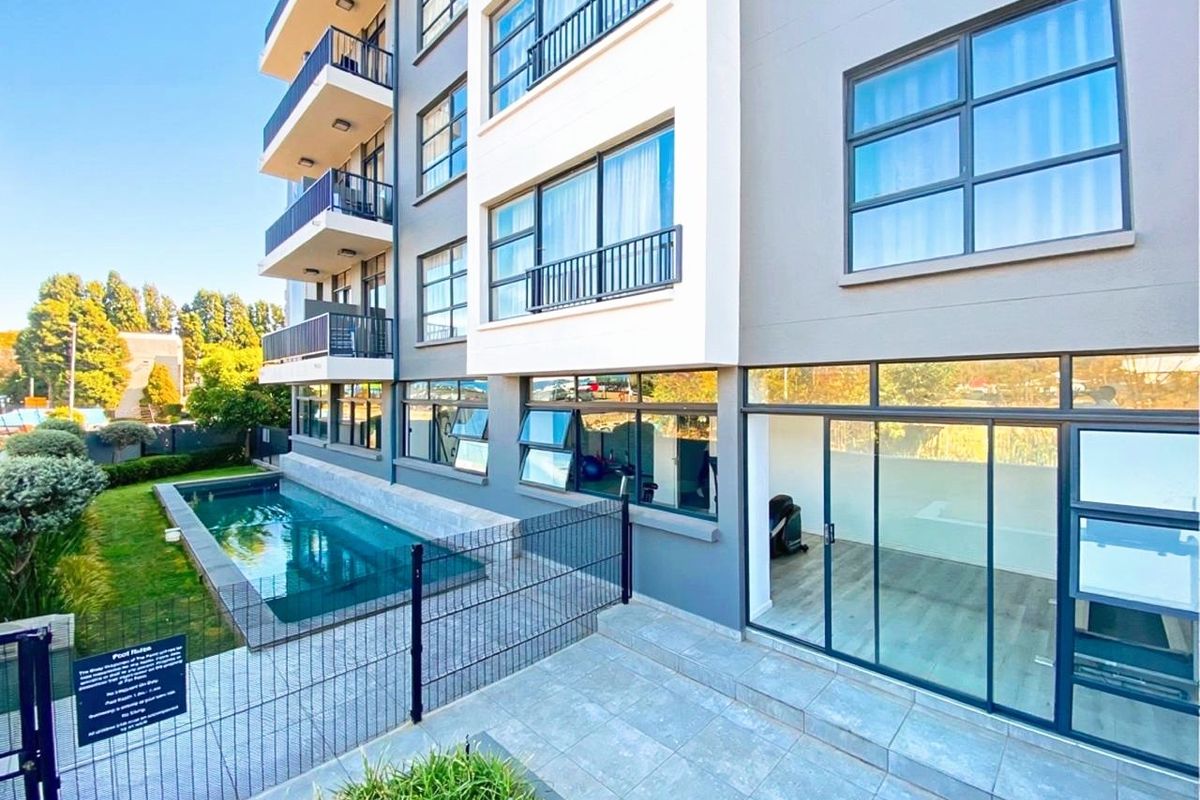 Exterior view of a modern apartment building featuring a swimming pool, ground floor patio access, and multiple balconies with metal railings.