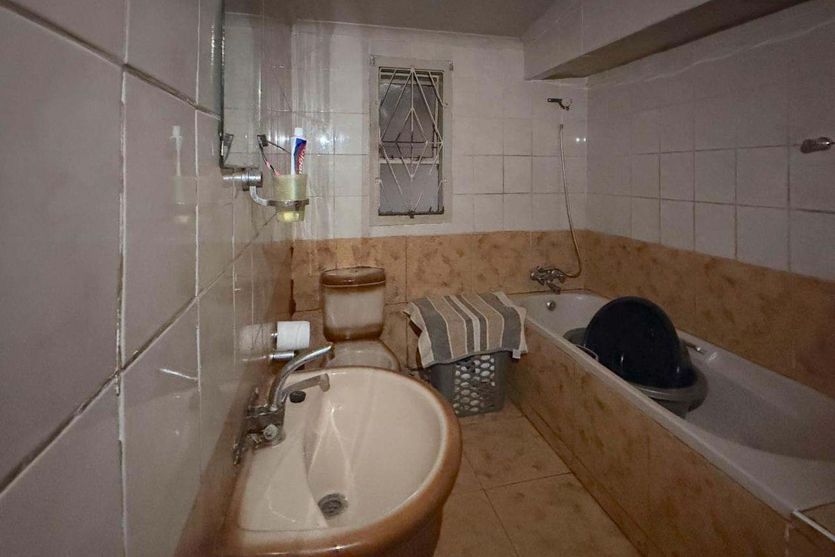 A dated bathroom featuring a wall-mounted basin, bathtub, and tiled finishes, requiring renovation to modernize the space.