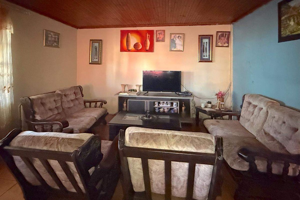 A living room featuring a timber tongue and groove ceiling and tiled flooring, requiring cosmetic updates to improve the overall aesthetic.