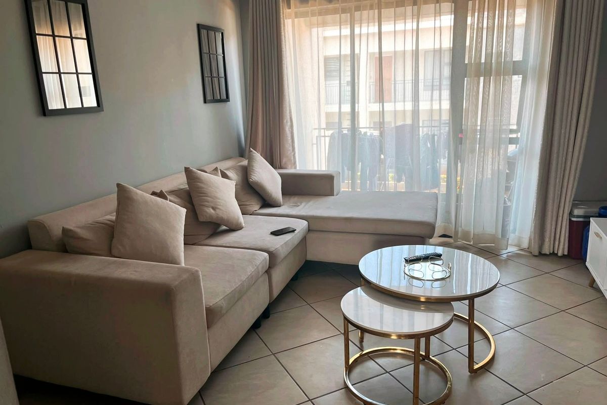 A well-lit living room featuring neutral tiled flooring and a large sliding glass door providing access to an outdoor balcony area.