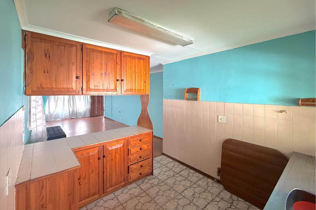 A dated kitchen featuring wooden cabinetry, tiled backsplash, and tiled flooring, offering a functional layout ready for modern renovation and cosmetic updates.