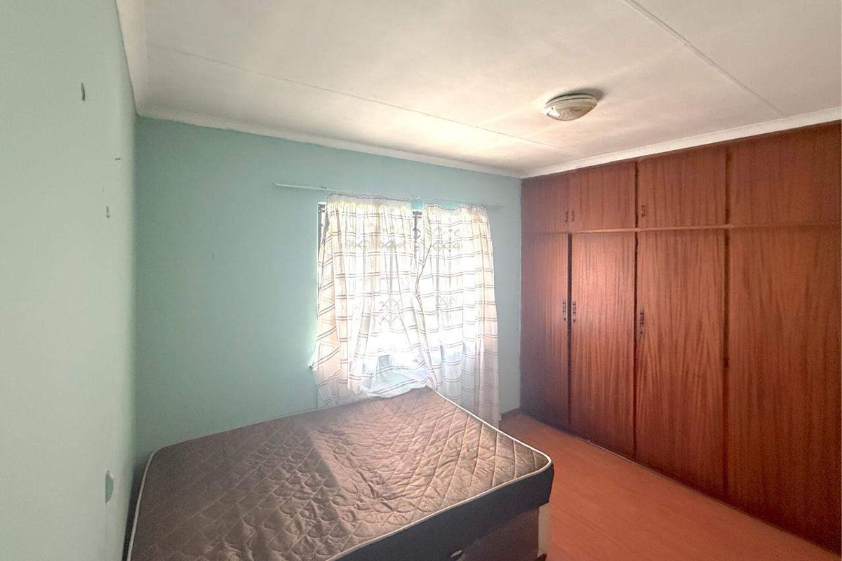 A bedroom featuring built-in wooden cupboards, laminate flooring, and a flush mount ceiling light, requiring some cosmetic updates to the walls and ceiling.
