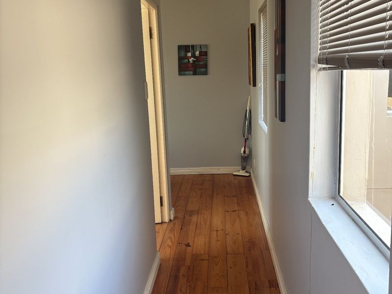 A well-maintained hallway featuring warm timber flooring, recessed downlighting, and natural light provided by a side window with fitted venetian blinds.