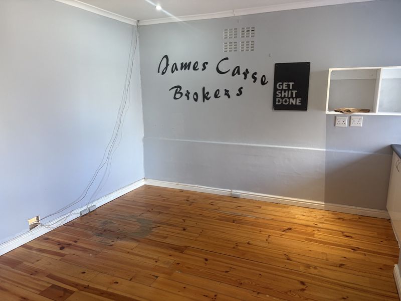 An empty office space featuring polished timber flooring, coving, and wall-mounted electrical points, suitable for a professional workspace.