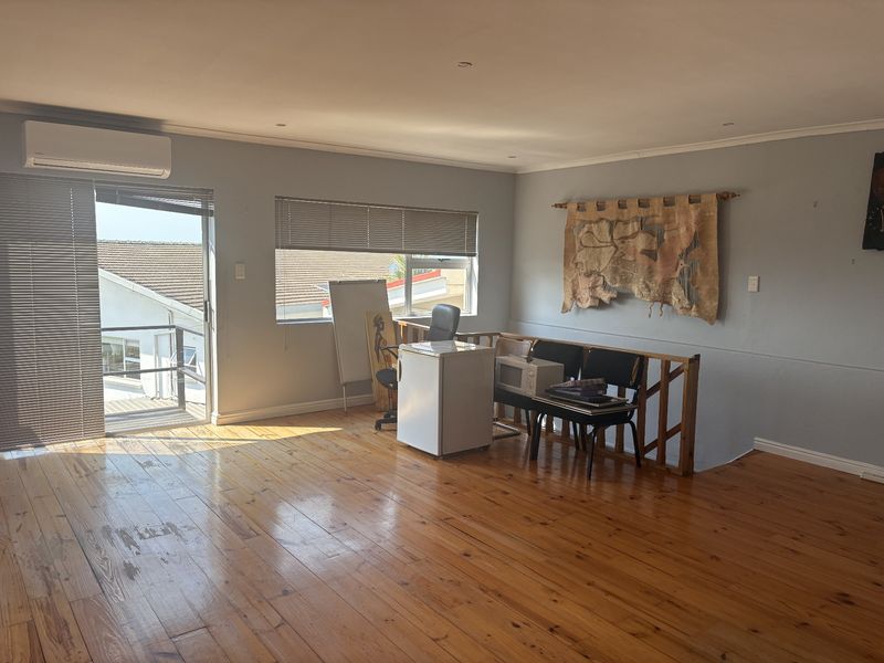 Spacious office area featuring polished hardwood flooring, a wall-mounted air conditioning unit, and access to an outdoor balcony through a sliding glass door.