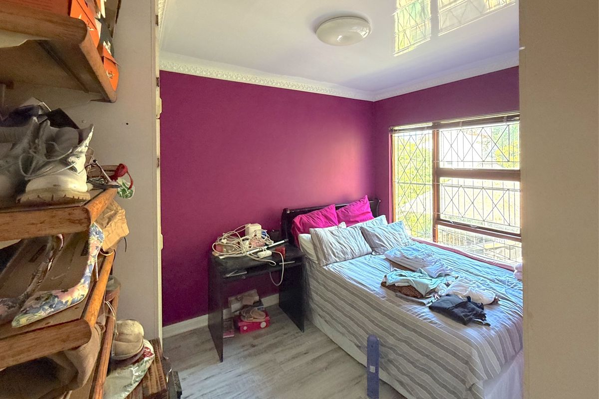 A compact bedroom featuring laminate flooring, decorative ceiling cornice, and security bars on the window.