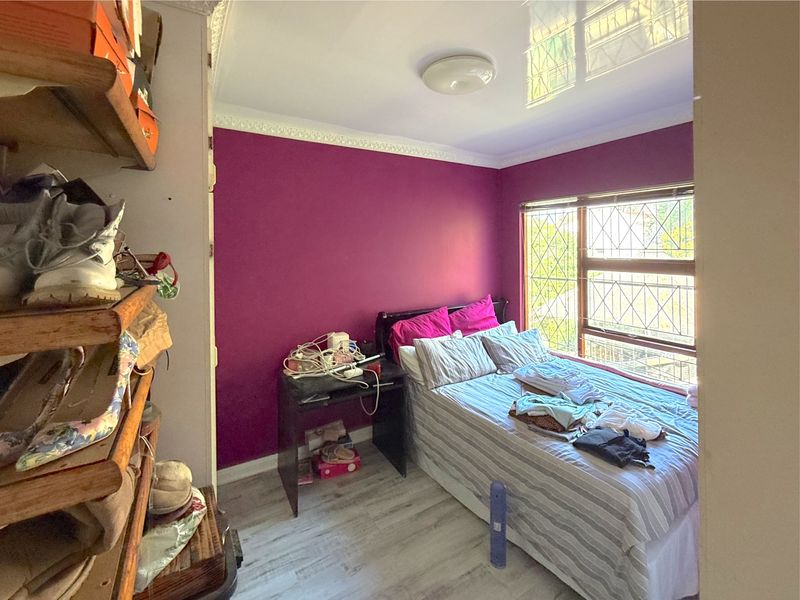 A compact bedroom featuring laminate flooring, decorative ceiling cornice, and security bars on the window.