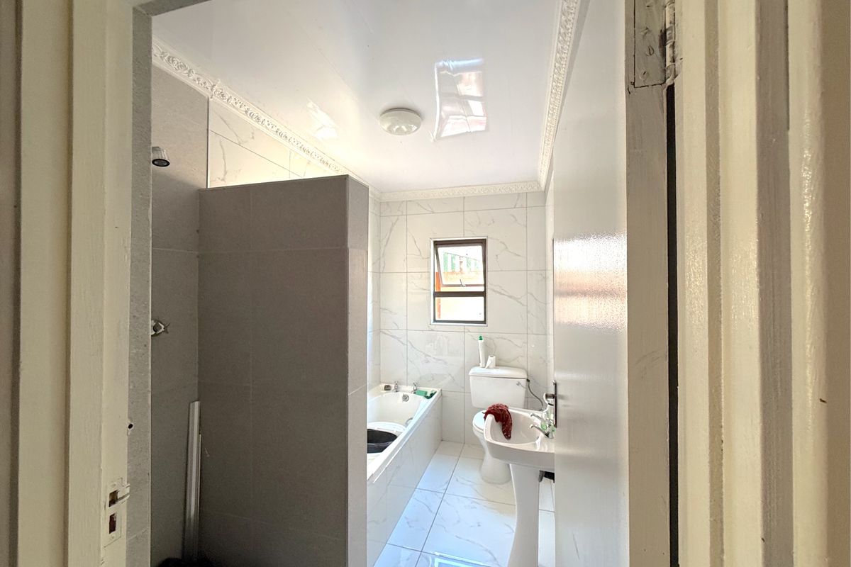 A clean, modern bathroom featuring a pedestal basin, toilet, and a built-in bathtub with shower combination, finished with white marble-look wall and floor tiles.