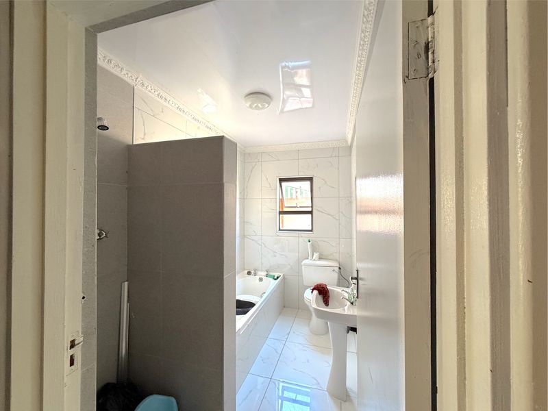 A clean, modern bathroom featuring a pedestal basin, toilet, and a built-in bathtub with shower combination, finished with white marble-look wall and floor tiles.