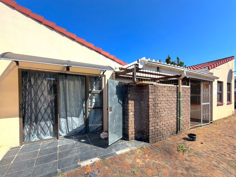 Rear exterior view featuring a paved patio area, sliding glass doors with security gates, and a brick-enclosed utility or storage space with metal security fencing.