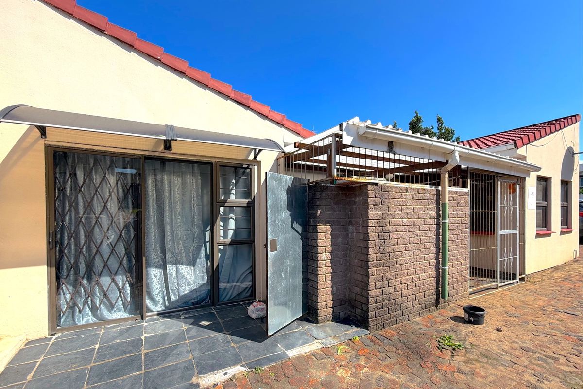 Rear exterior view featuring a paved patio area, sliding glass doors with security gates, and a brick-enclosed utility or storage space with metal security fencing.