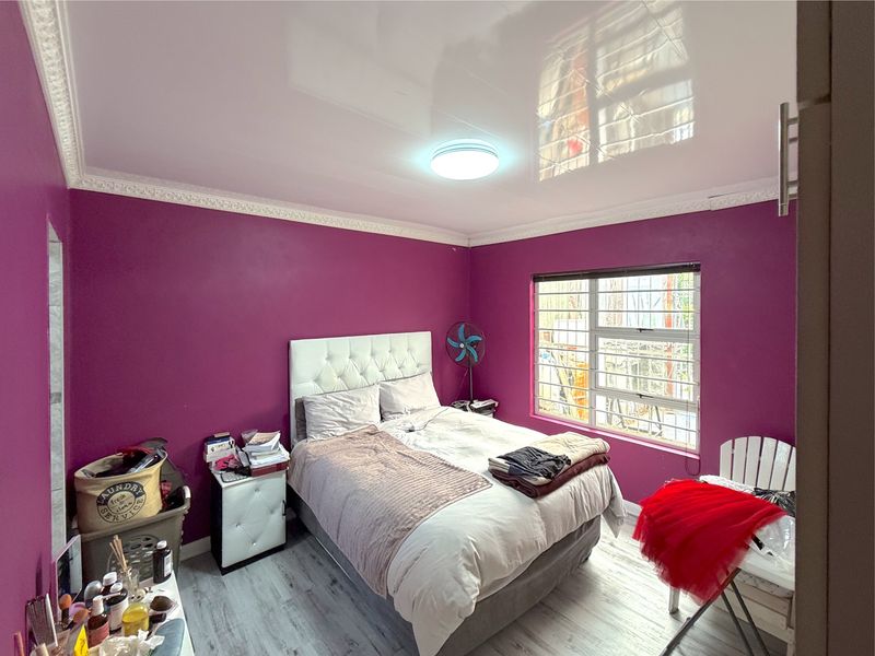 A bedroom featuring a high-gloss stretch ceiling, decorative crown molding, laminate flooring, and a window fitted with security bars.