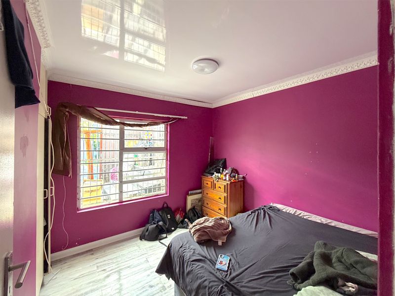 A bedroom featuring laminate flooring, a glossy ceiling with decorative cornice, and security bars on the window.
